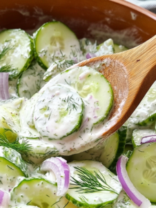 Add the sliced cucumbers, red onion, and chopped fresh dill to the dressing. Toss gently to coat everything evenly.