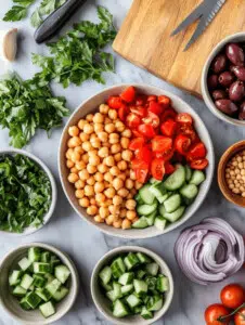 In a large mixing bowl, combine the chickpeas, cherry tomatoes, cucumber, red bell pepper, red onion, Kalamata olives, parsley, and mint. Toss gently to mix.