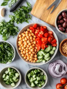 In a large mixing bowl, combine the chickpeas, cherry tomatoes, cucumber, red bell pepper, red onion, Kalamata olives, parsley, and mint. Toss gently to mix.
